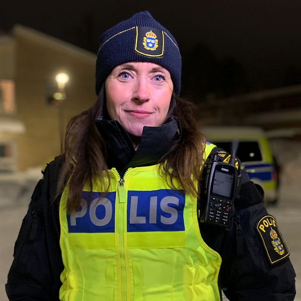 En polis utomhus i mörkret med en polisbuss i bakgrunden