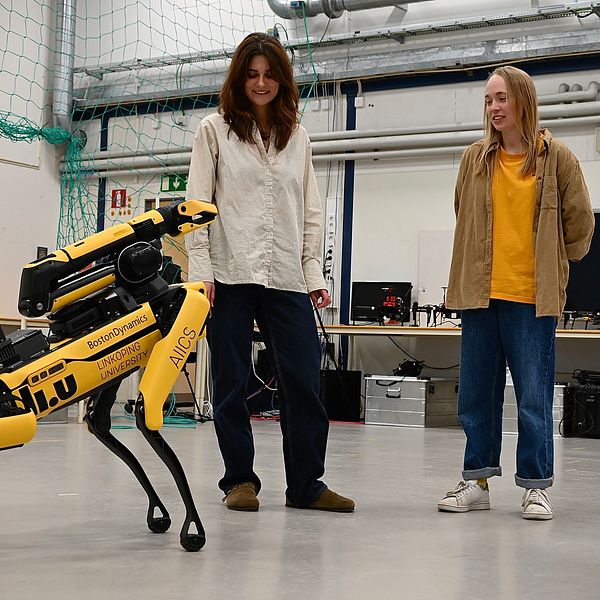 Två personer tittar på en gul fyrbent robot i ett laboratorium.