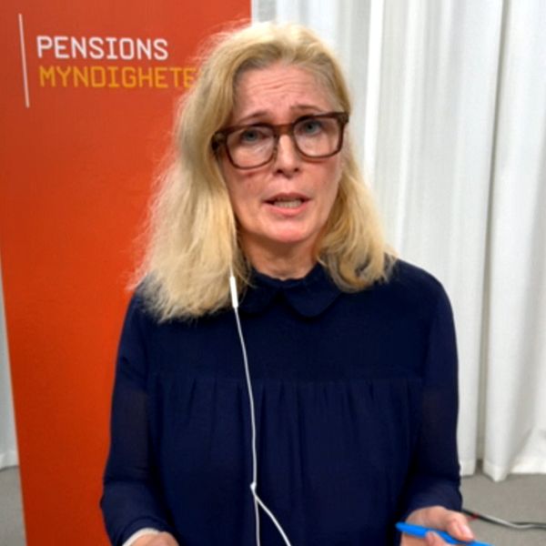 Katharina Hultberg står framför en orange bakgrund med texten ”Pensionsmyndigheten”. Hon har hörlurar på sig och håller i en penna.