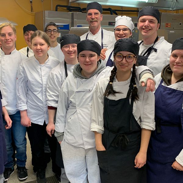 Elever och lärare står i kockkläder i restaurangköket på Ljungbergsgymnasiet i Borlänge.
