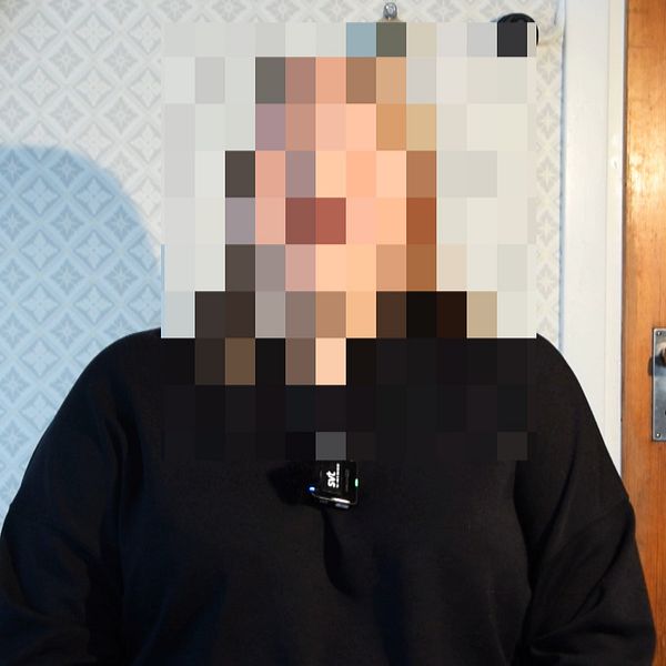 En person med pixlat ansikte framför en dörr och vitmönstrad tapet.