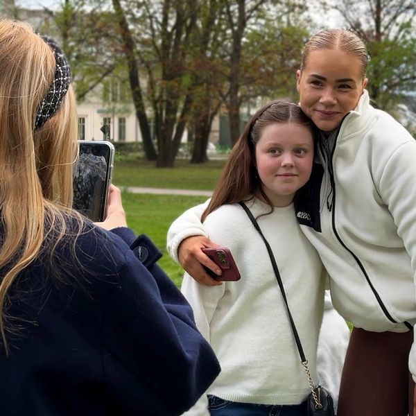 En person fotograferar två personer som poserar tillsammans i en grönskande park.