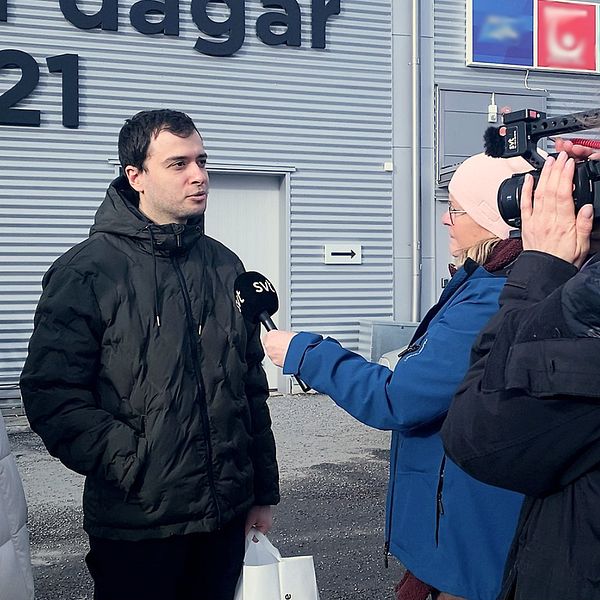 Reporter intervjuar två personer utanför en byggnad.