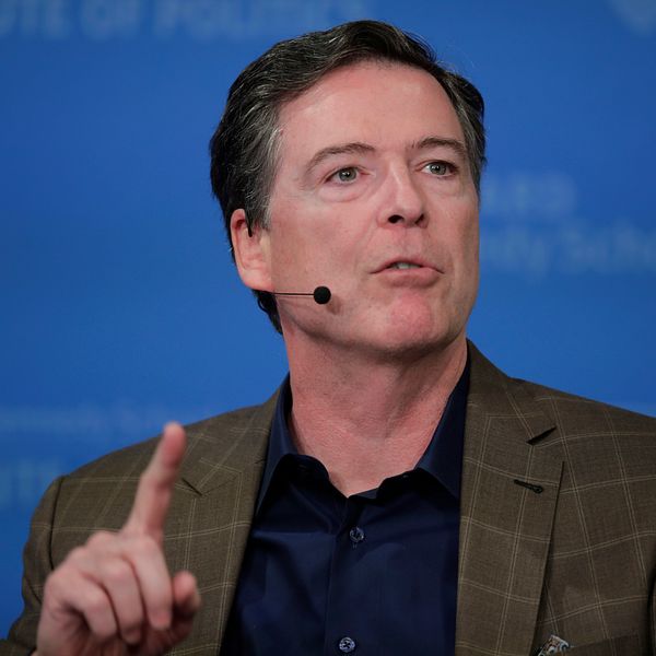 James Comey talar och pekar med ett finger framför blå bakgrund