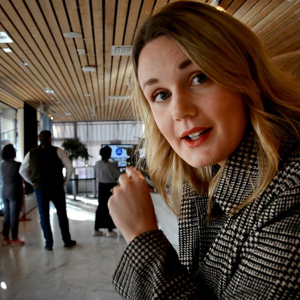 En reporter står i stadshuset, bakom ser man en samling av människor.
