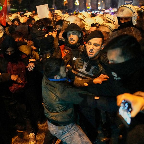 Folkmassa i demonstration, upplopp mellan protesterande och poliser med hjälmar och sköldar.
