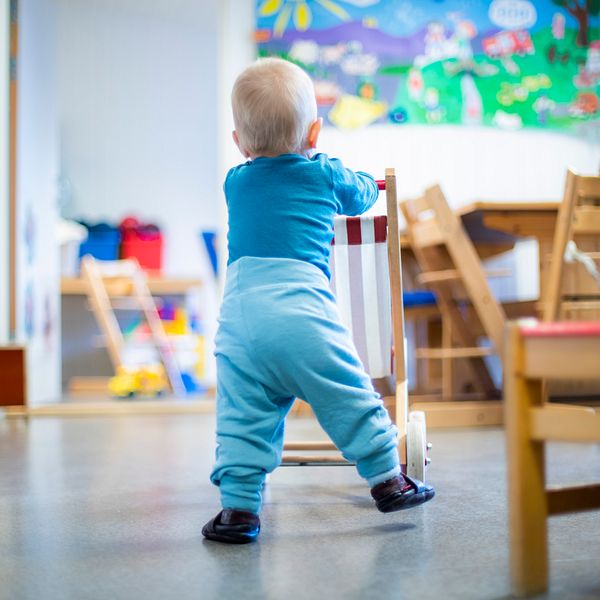 Liten pojke står i ett förskolerum och tittar mot en färgglad tavla