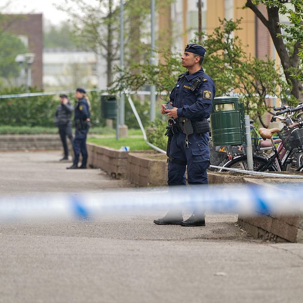 Poliser bevakar ett avspärrat område utanför ett bostadshus.