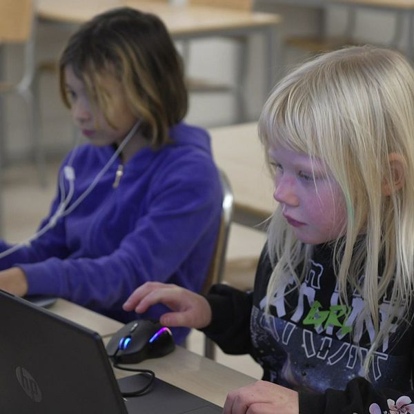 två barn sitter i ett klassrum med varsin bärbar dator