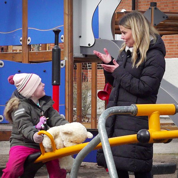 Mamma pratar teckenspråk med sitt barn på en lekplats.