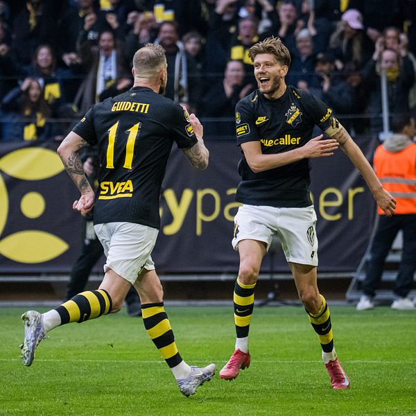 Två AIK-spelare firar mål inför jublande supportrar på fotbollsläktaren.