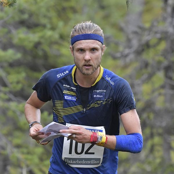Man springer orientering i skog med karta och nummerlapp.