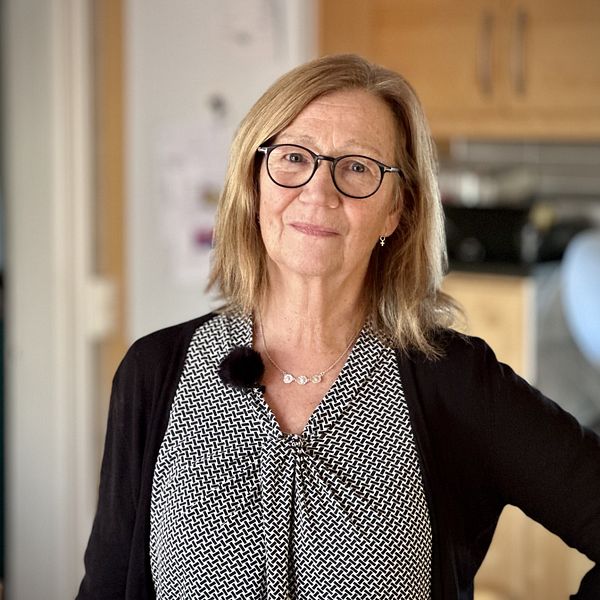 En nöjd Birgitta Sjölin hemma vid sitt kök blickar in i kameran.