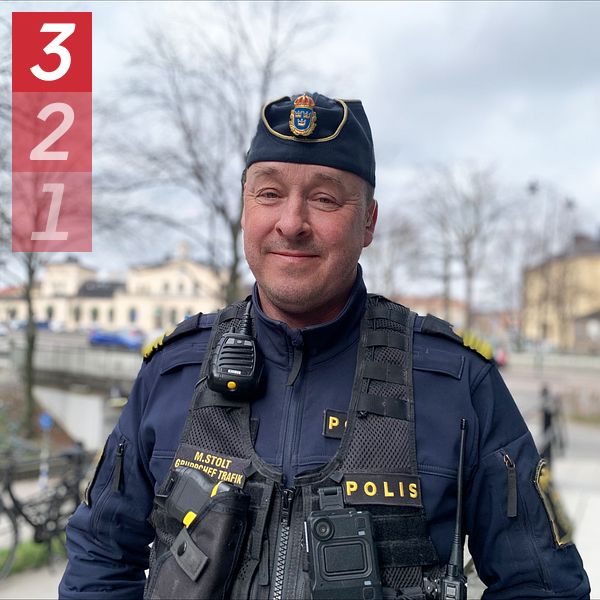 Polis med uniform och utrustning i stadsmiljö. Bakgrund med park och byggnader.