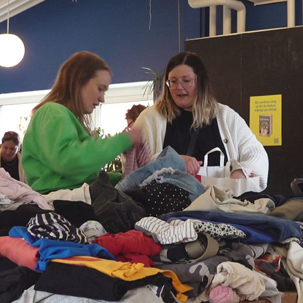 två kvinnor står och kollar bland kläder på en klädbytardag