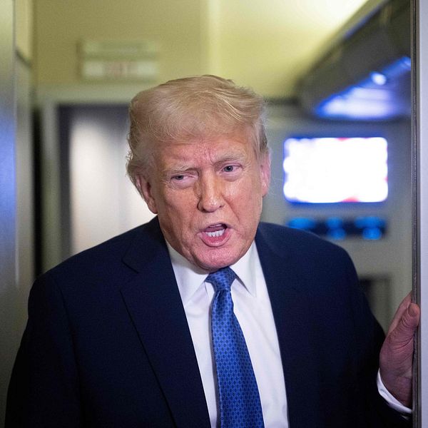 Donald Trump med tv-skärm synlig i bakgrunden.