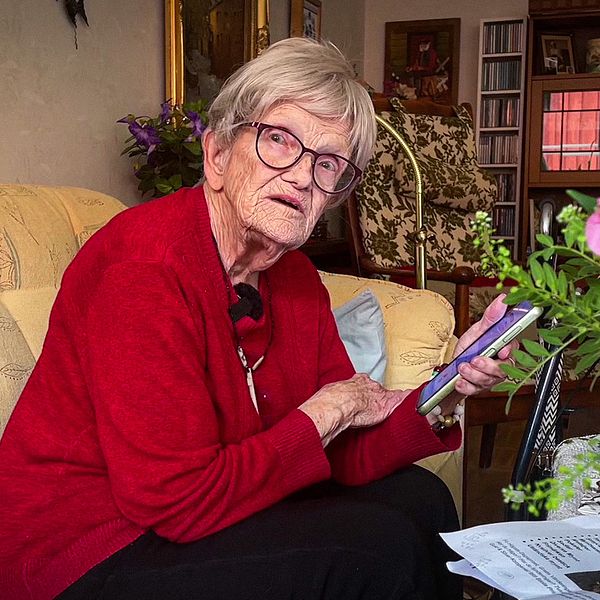 87-åriga Kirsten sitter i en soffa i sitt hem och håller i en mobiltelefon.