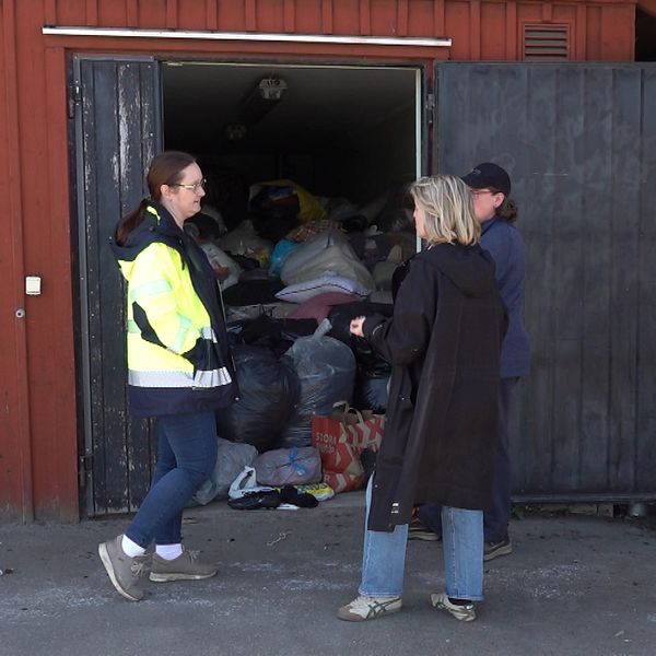 Tre personer står framför ett förråd fyllt med insamlade kläder och saker.