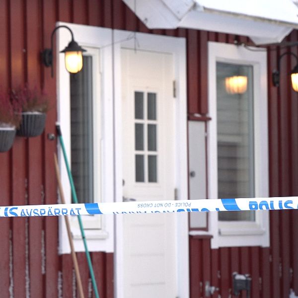 Ett rött trähus med snö på marken och blåvit polisavspärrning framför ingången.