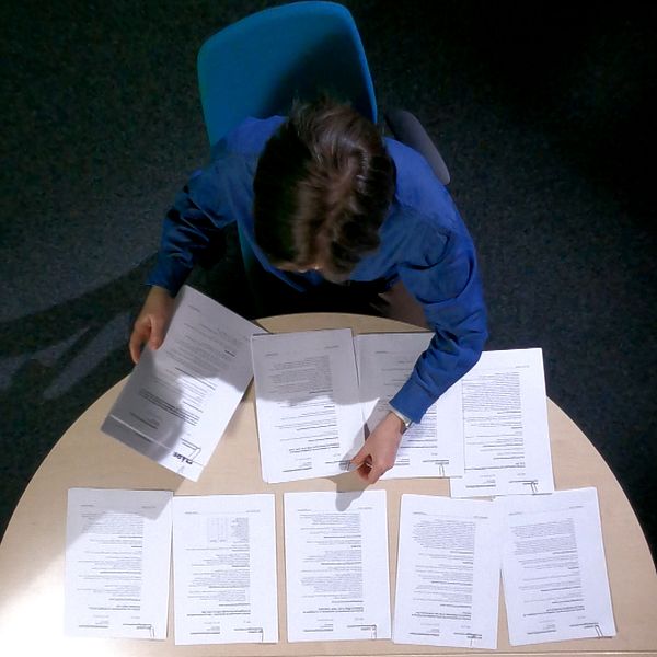 En kvinna i blå skjorta lägger ut flera A4 papper på ett bord.