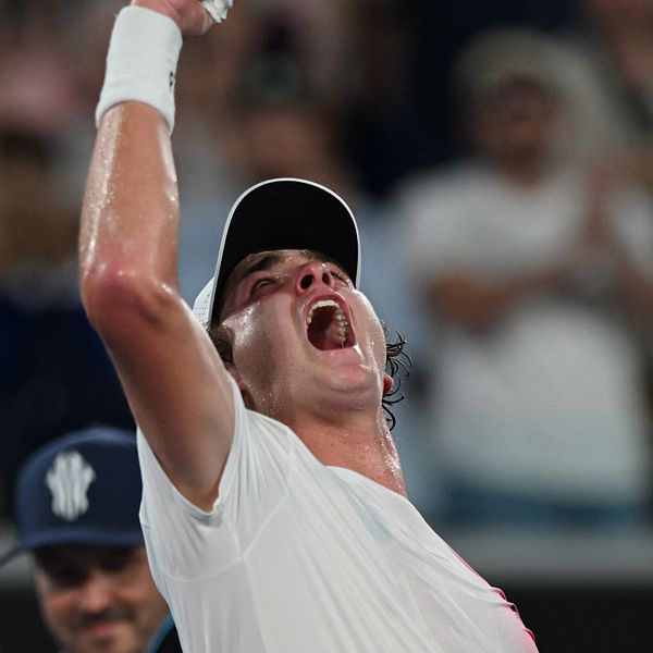 En tennisspelare firar triumferande med uppsträckt arm efter en viktig poäng under en match. Bakgrunden visar en entusiastisk publik som hejar.