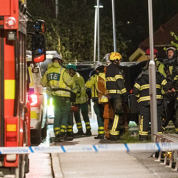 Räddningstjänst arbetar vid avspärrat område på gata, brandbil synlig till vänster.