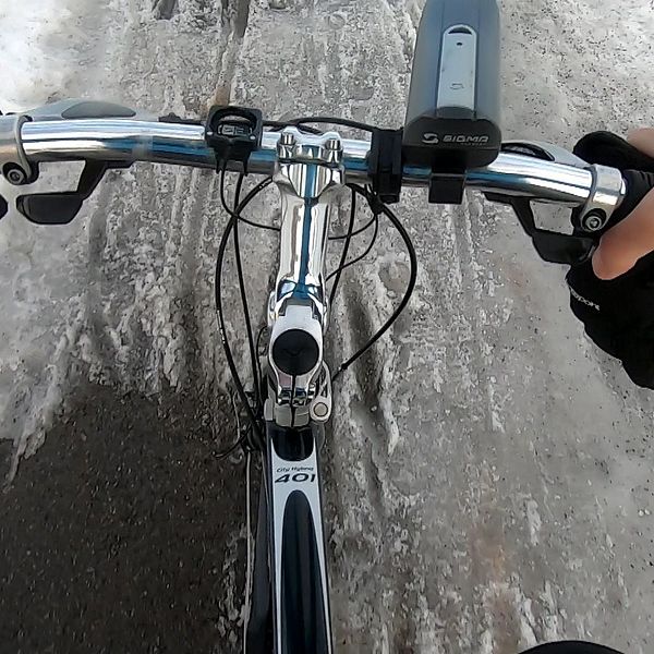 Händer på cykelstyre som färdas på en slaskig cykelväg.