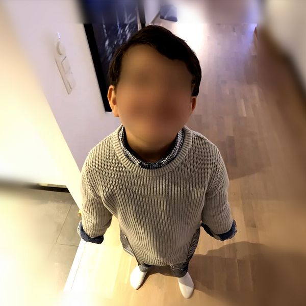 Barn i vit tröja fotograferad från ovan i ett rum med trägolv.