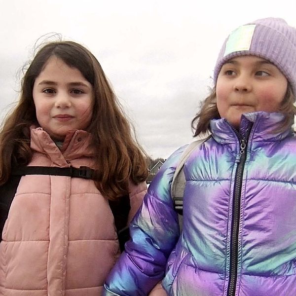 Två flickor står vända mot kameran intill en snötäckt idrottsplan