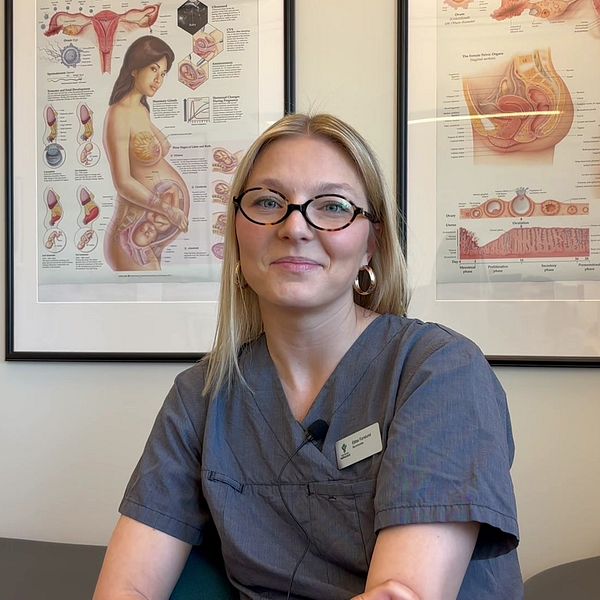 Person i medicinsk uniform framför anatomiska planscher.