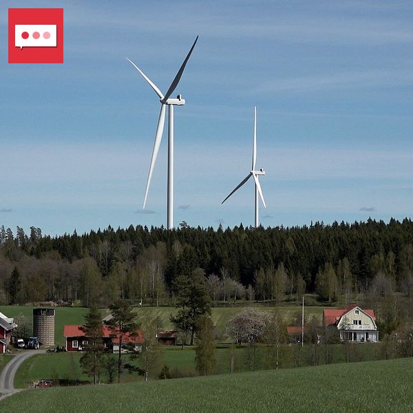 Flera vindkraftverk bakom gårdar och åkermark i lantlig miljö.