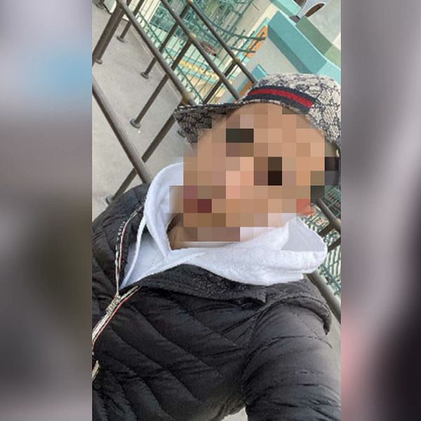 Person med pixlat ansikte framför oskarp bakgrund av byggnader.