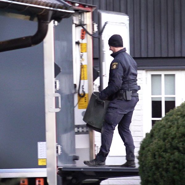 En polis från Nationella bombskyddet bär en tunna och går in i en lastbil vid en byggnad, omgiven av grönska.
