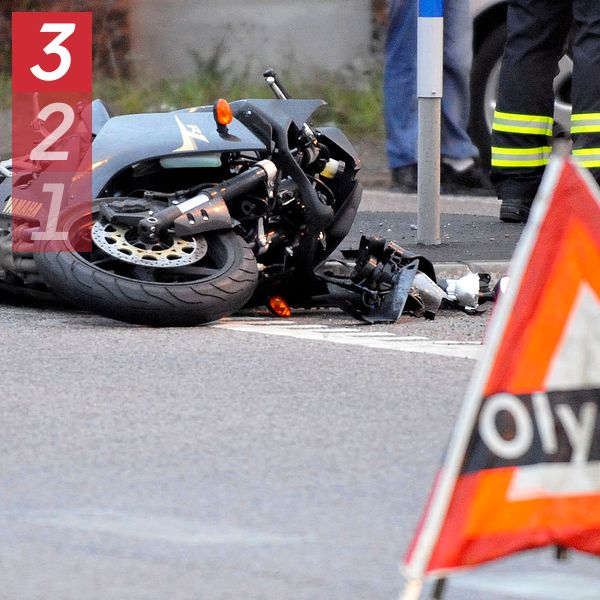 Omkullvält motorcykel, olycksvarningstriangel i förgrunden, brandmän i bakgrunden.