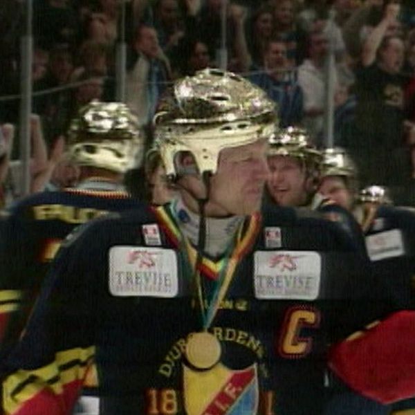 Ishockeyspelare med guldhjälm och medalj firar seger inför publik.