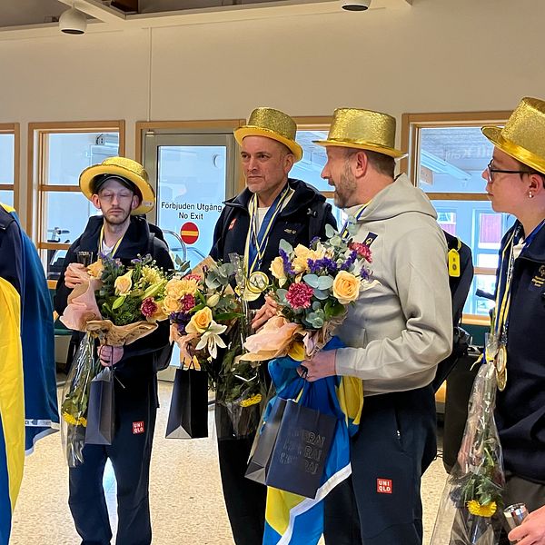 Fem personer med guldhattar står i grupp och håller blommor.