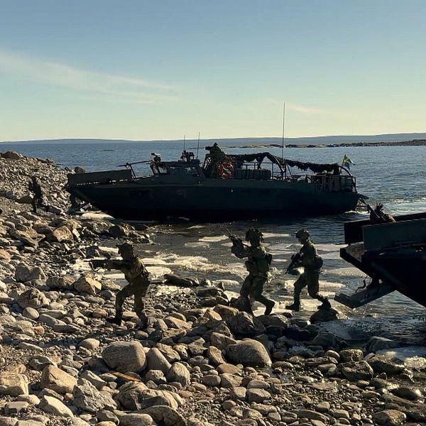 Soldater stiger i land från militärbåtar vid stenig kust.