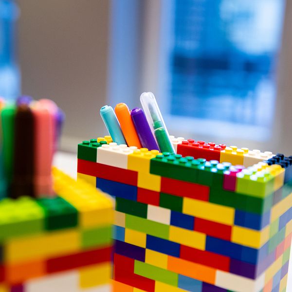 Färgglada pennhållare byggda av legobitar med pennor i, under ett fönster.
