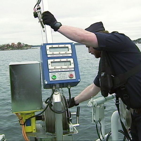 Man ombord på båt står vid relingen och håller i sjömätningsinstrument över vattenytan.