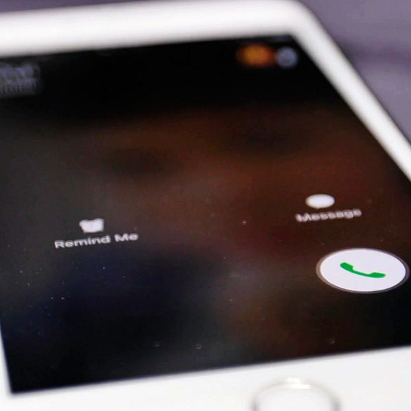 Skärmen på en smartphone som visar en inkommande samtalsmeny med alternativet ”Remind Me”, ”Message” och en grön telefonikon för att svara på samtalet. En hand är i färd med att trycka på telefonikonen.