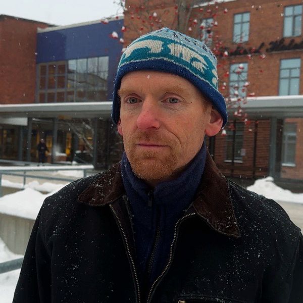 En person står framför Karlstad centralsjukhus med flera fönster och snö på marken. I bakgrunden syns en gul buss och en del av en annan byggnad med en skylt. Det är vinter och snöigt.