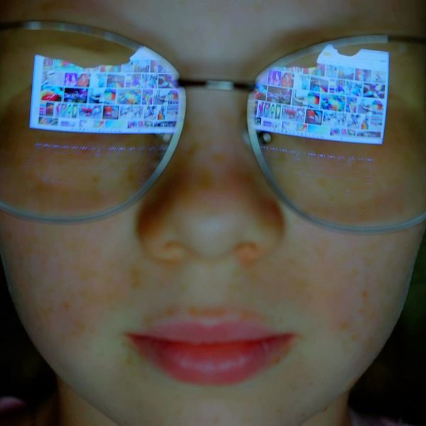 Närbild flicka med glasögon där bildskärm med foton från sociala medier speglas.