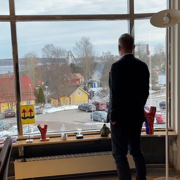 Person står vid fönster och blickar ut över snöigt stadslandskap.