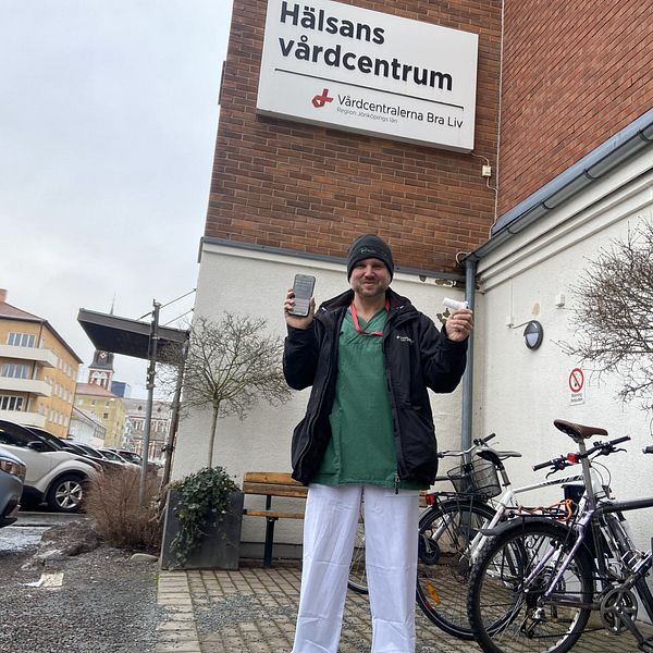 Ulf Österstad står utanför Hälsans vårdcentrum i Jönköping och håller i astmatekniken i ena handen och en mobiltelefon i den andra.