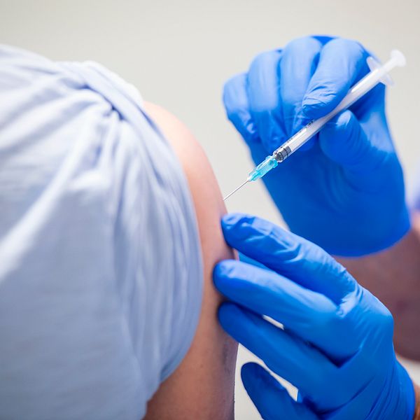 En sjukvårdspersonal ger en vaccination genom att injicera en spruta i en patients arm, där patientens hud är synlig. Sjukvårdspersonalen bär blå handskar.