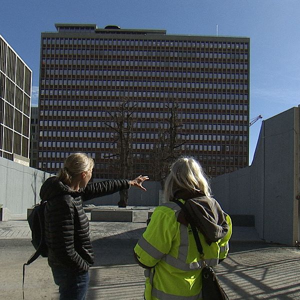 Två personer diskuterar framför ett stort kontorshus under en klarblå himmel.