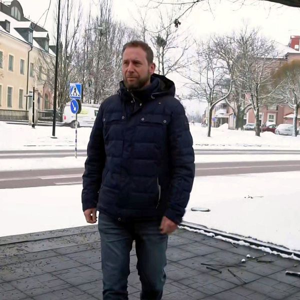 en skolchef som går på en gata med hus bakom , snömiljö runtom.