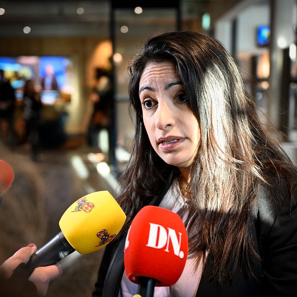 Person intervjuas av flera reportrar med mikrofoner från SVT och DN i en offentlig miljö.