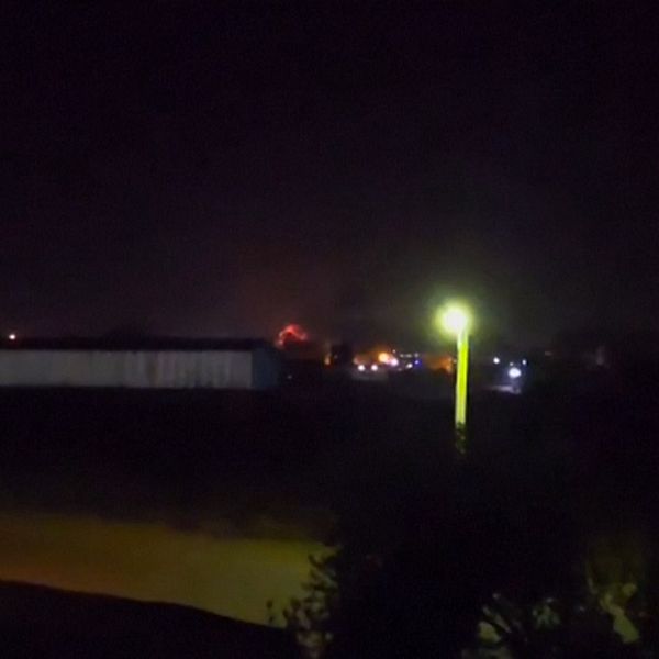 Ljus från en brand syns i fjärran bakom byggnader under natten.