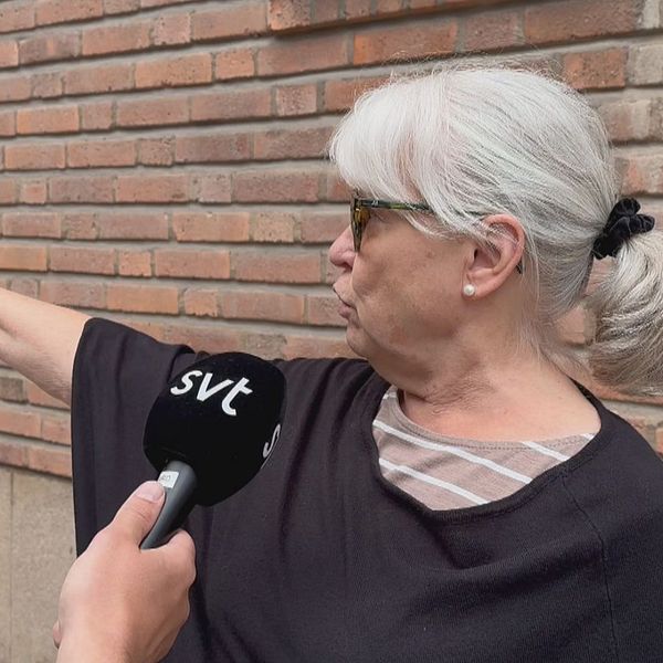 äldre kvinna som blir intervjuad pekar med högerarmen